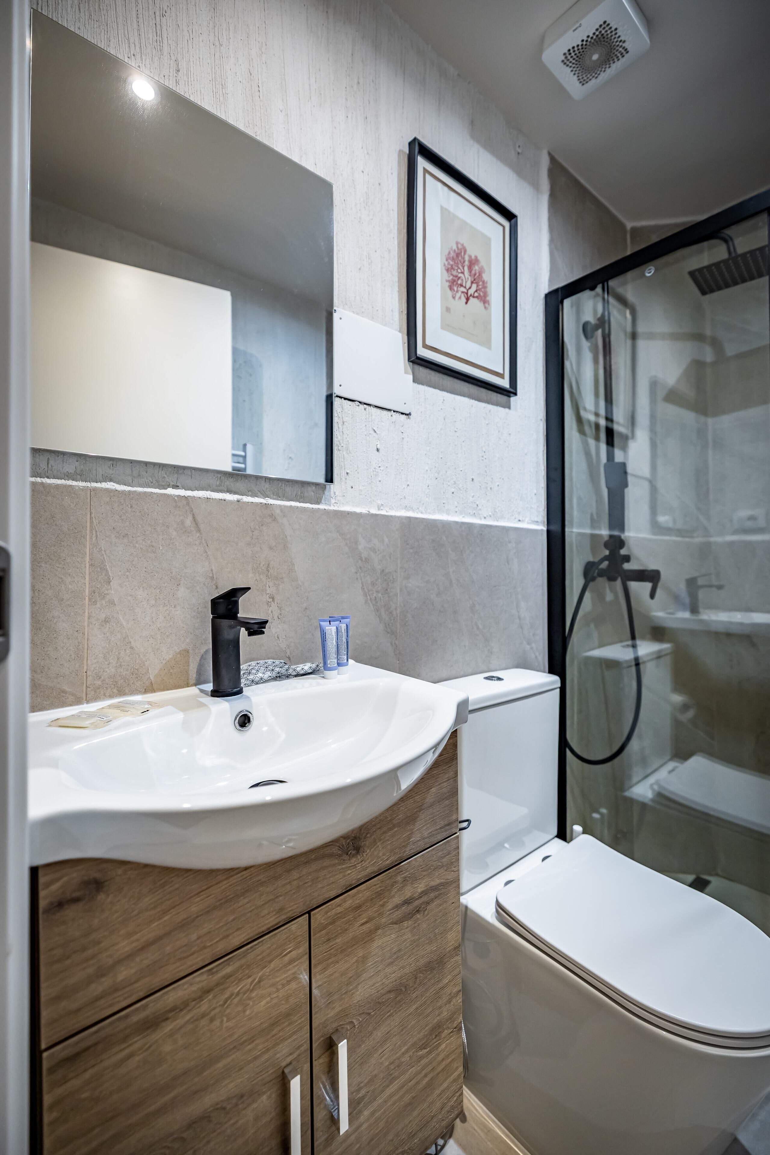Ein modernes Badezimmer mit Waschbecken, Holz-Waschtisch, einem gerahmten Bild an der Wand und einer Duschkabine.