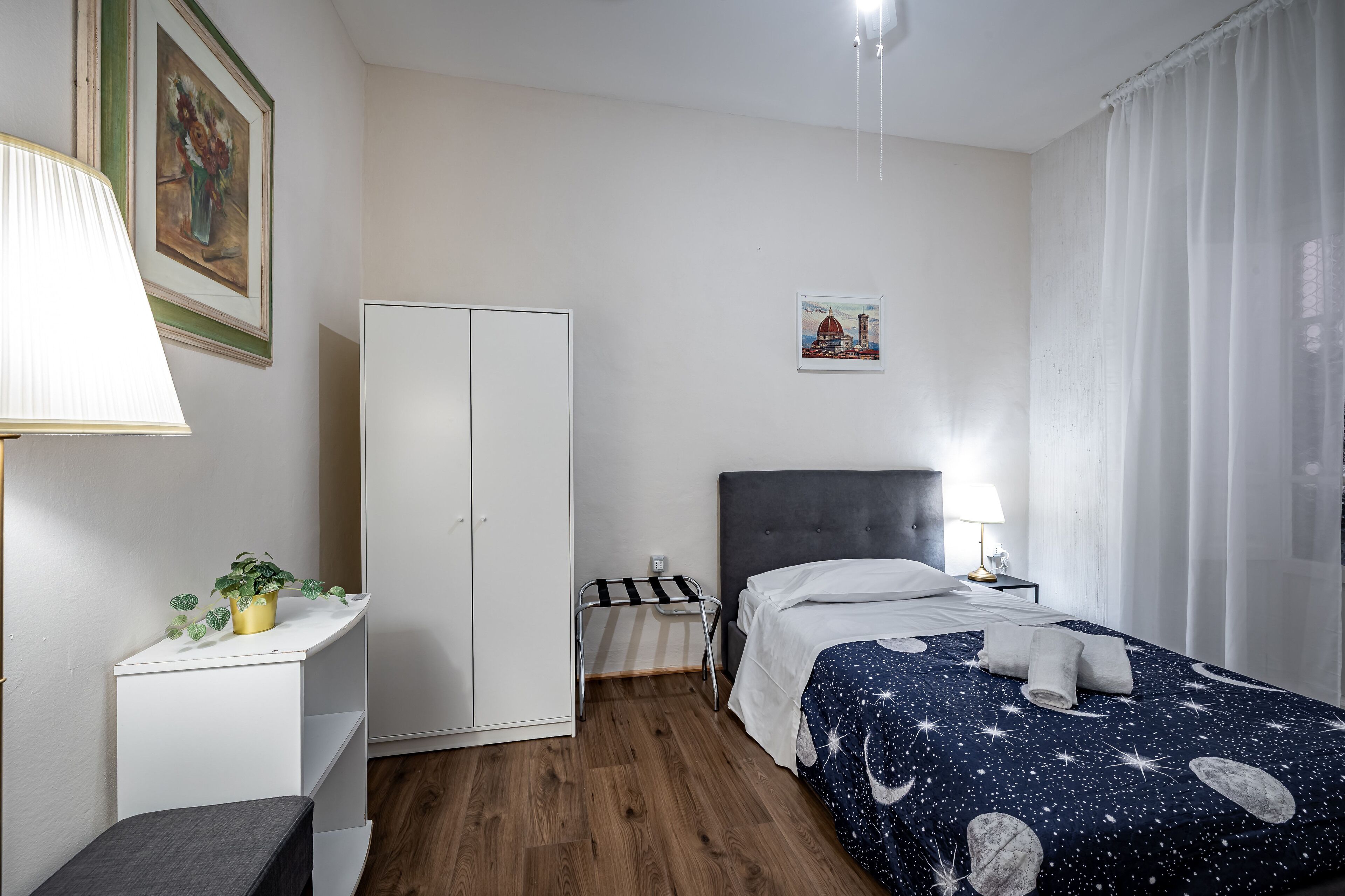 Ein Schlafzimmer mit einem Bett, einem Kleiderschrank, einem Schreibtisch mit Lampe und einer kleinen Pflanze.