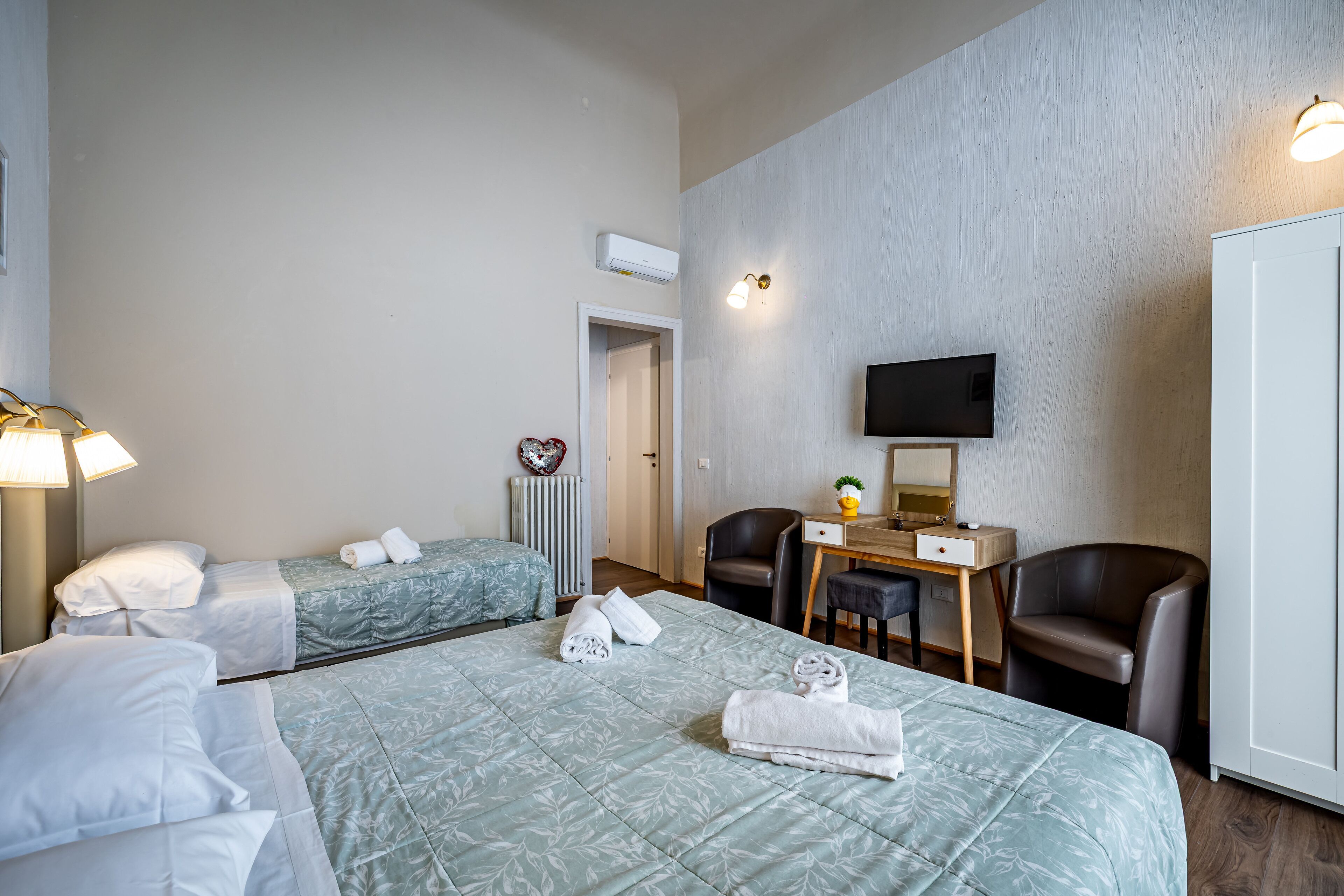 Ein Hotelzimmer mit zwei Betten, einem Schreibtisch mit Stuhl, einem Fernseher und einer Heizung.