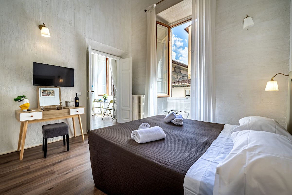 A hotel room with a bed, a desk, a television, and a view of the outside.
