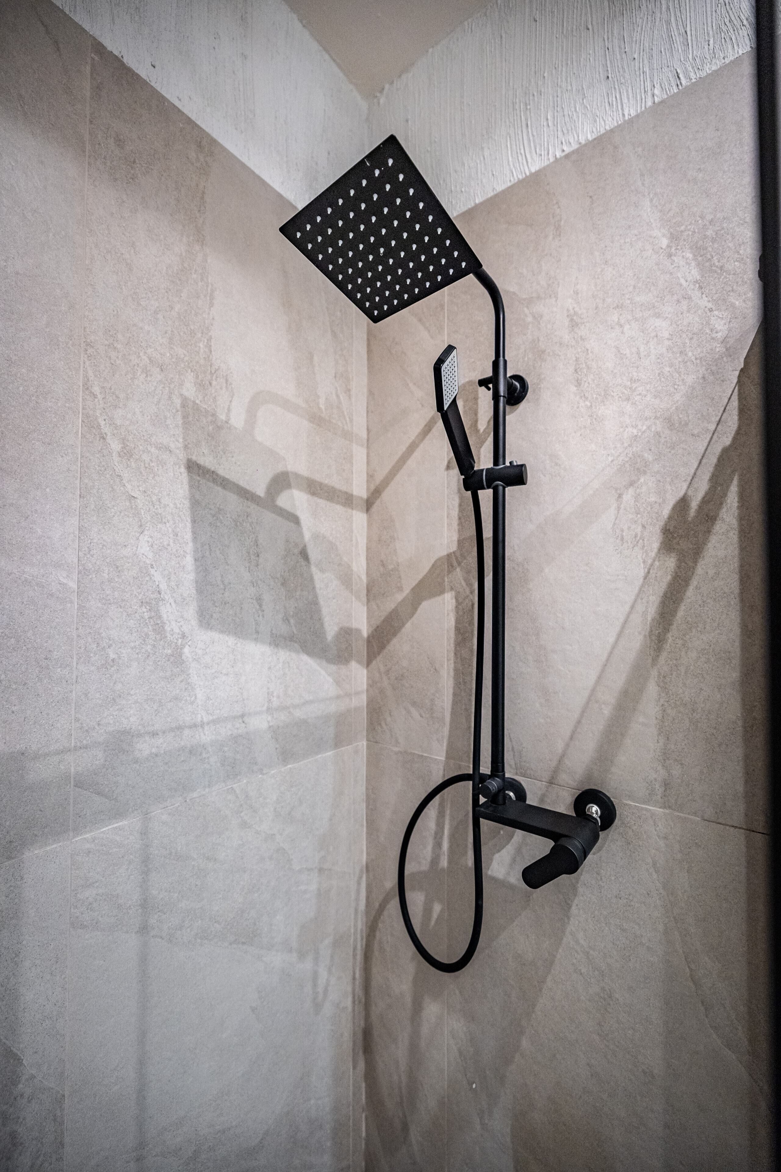 A shower with a square head and a handheld attachment, mounted on a tiled wall.