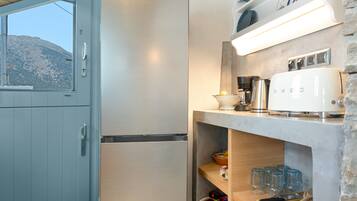 Una cocina compacta con un refrigerador de acero inoxidable, una tetera eléctrica blanca y un tostador sobre una repisa.
