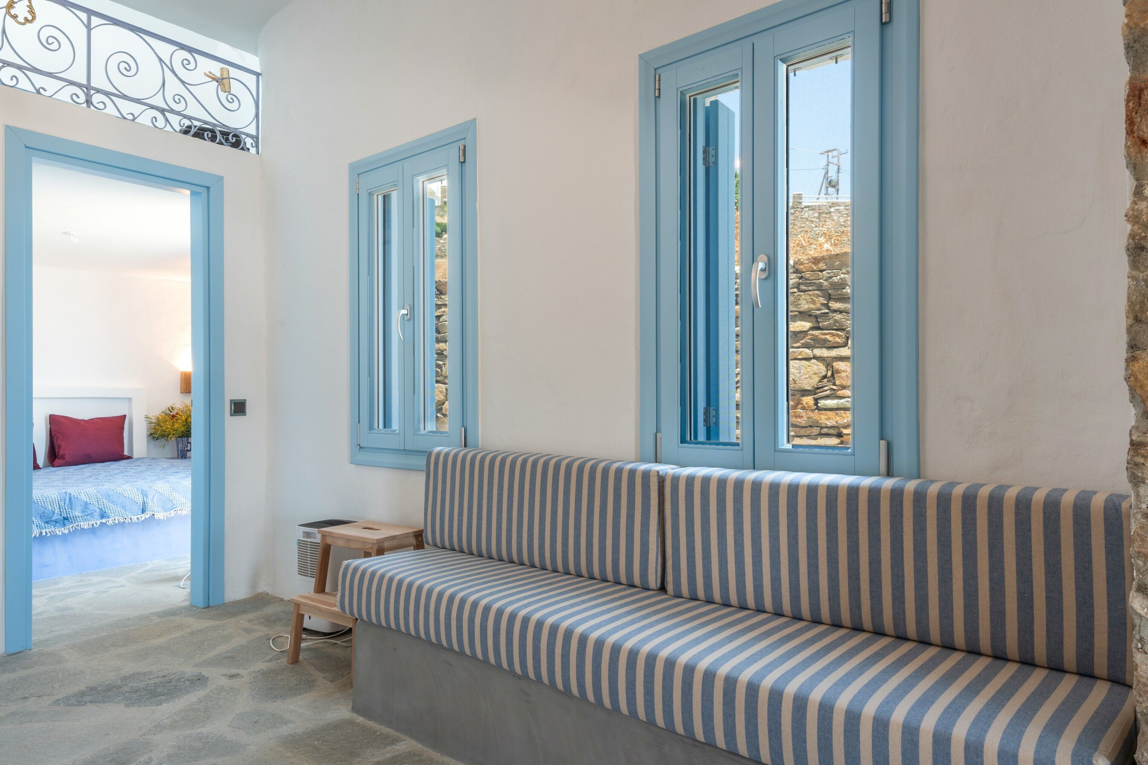 Una habitación con un sofá a rayas, una cama con almohada roja y una pared de piedra.