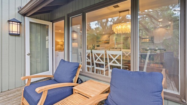 A covered outdoor seating area with two wooden chairs and a table, a glass door leading to an interior space, and a hanging light fixture. - Fairway Oaks Villa! Lagoon views! Short 5-7 minute stroll to the beach! (Kiawah Island)