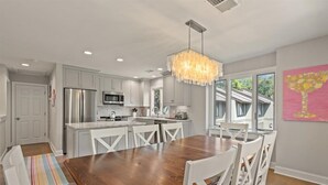 A modern kitchen with white cabinetry, a stainless steel refrigerator, and a wooden dining table with white chairs. - Fairway Oaks Villa! Lagoon views! Short 5-7 minute stroll to the beach! (Kiawah Island)