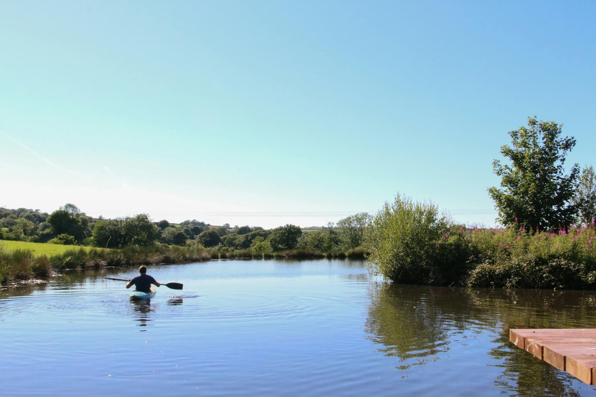 Ein ruhiger Fluss mit einer Person im Kajak, umgeben von Grün und einem klaren Himmel.