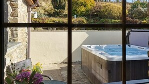 A hot tub in a garden with stone walls and a view of trees and bushes. - Y Dderwen, Aberaeron (Llanarth)