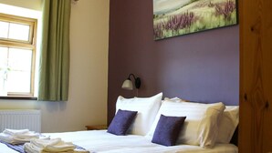 A neatly made bed with white and purple pillows, a lamp, and a painting of a field on the wall. - Y Dderwen, Aberaeron (Llanarth)