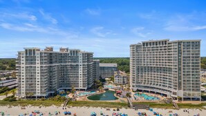A resort with high-rise buildings, a central pool area, and a beach with umbrellas.