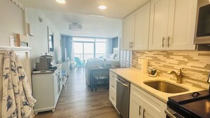A modern kitchen with white cabinets, a stainless steel sink, and a large window overlooking a balcony.