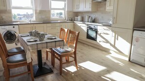 A kitchen with a dining table set for four, wooden chairs, a washing machine, an oven, and a refrigerator.