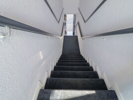 Uma escadaria com corrimão, degraus carpetados e paredes brancas.
