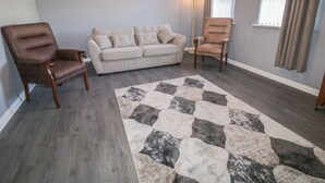 A living room with a grey sofa, two armchairs, a patterned rug, and a painting on the wall.