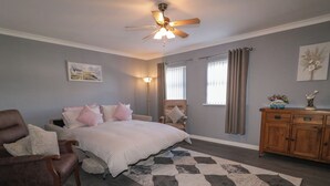 A bedroom with a bed, a chair, a wooden dresser, a ceiling fan, and a rug.