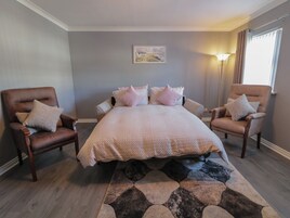 Quarto com uma cama grande, duas poltronas, um tapete e um quadro na parede.