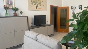 Een woonkamer met een bank, een televisie, een kast en een deur naar een andere kamer.