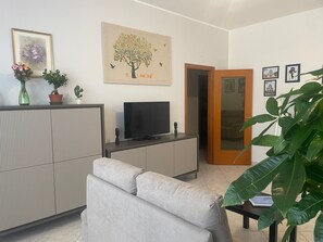 Una sala de estar con un sofá, un televisor, un mueble y una puerta que da a otra habitación.