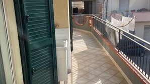 Een balkon met een groene deur, betegelde vloer en uitzicht op omliggende gebouwen.