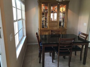 A dining area with a glass-top table surrounded by wooden chairs, a wooden cabinet with glass doors, and a window providing natural light.