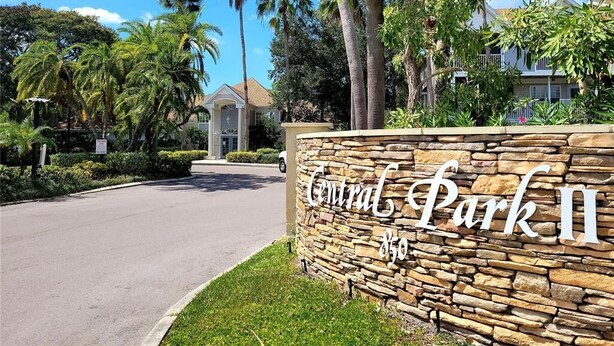 A stone wall with "Central Park II" signage, a paved road, and palm trees.