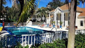A swimming pool surrounded by lounge chairs and palm trees, with a house in the background.