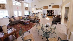 A spacious living room with a sofa, coffee table, and chairs, a dining area with a glass table, and a kitchen in the background.