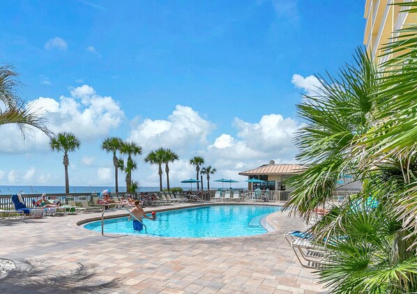 A pool area with lounge chairs and palm trees, overlooking a body of water.