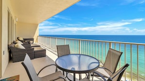 Un balcón con una mesa redonda de cristal y cuatro sillas, con vista a un mar azul y despejado.