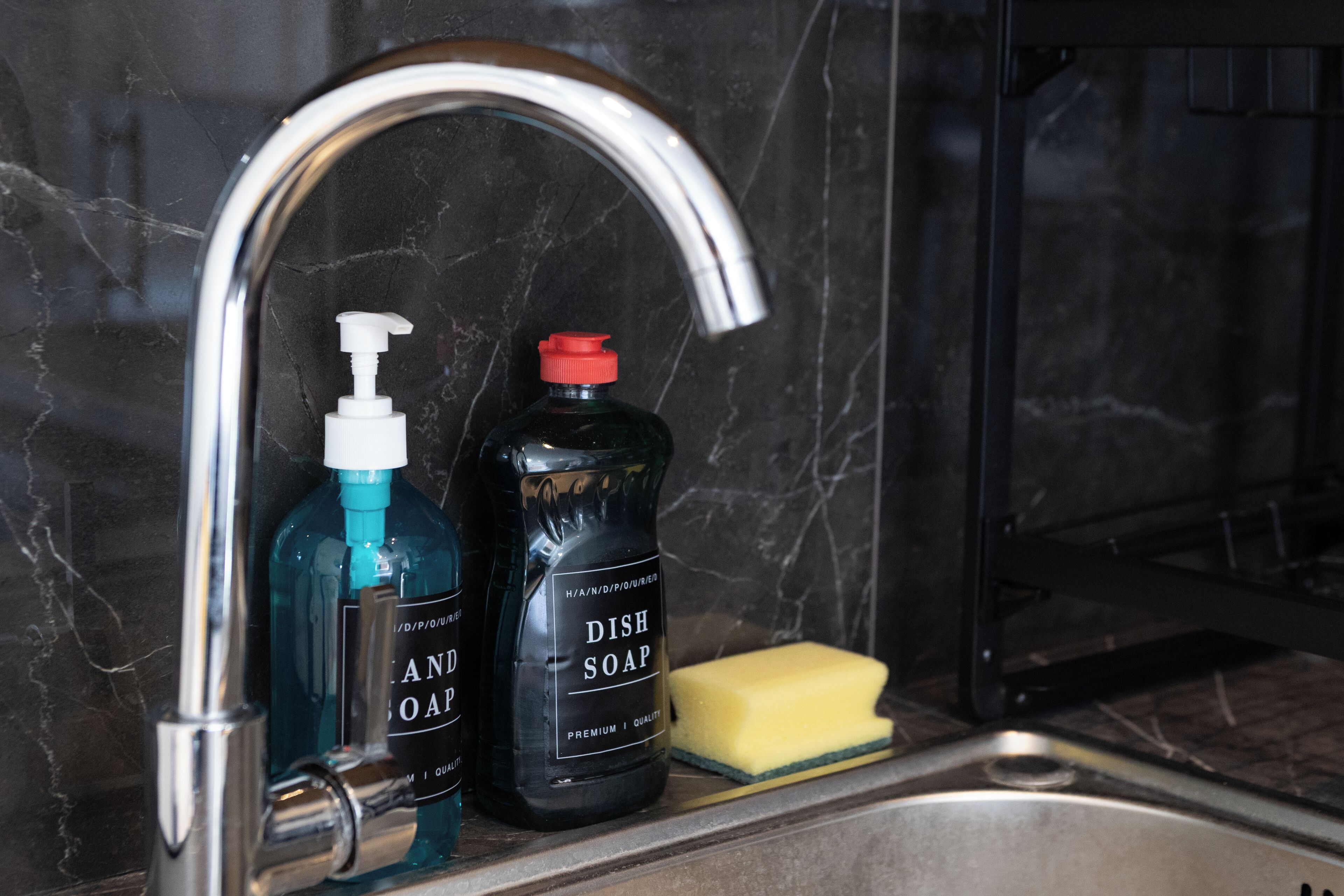 A kitchen sink with a faucet, a bottle of hand soap, and a sponge.