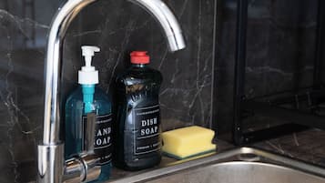 A kitchen sink with a faucet, a bottle of hand soap, and a sponge.