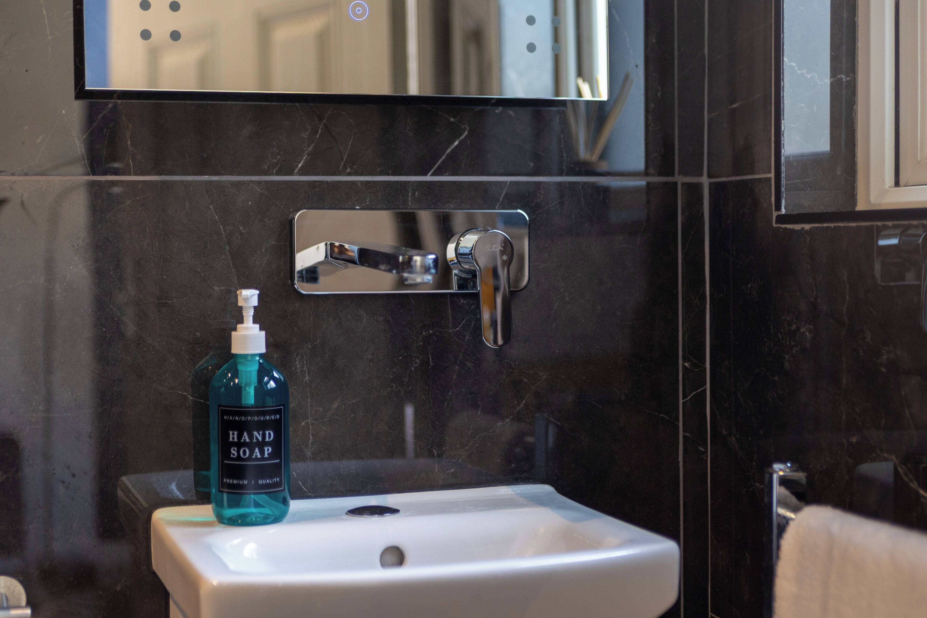 A bathroom with a white sink, a mirror above it, and a bottle of hand soap on the sink.
