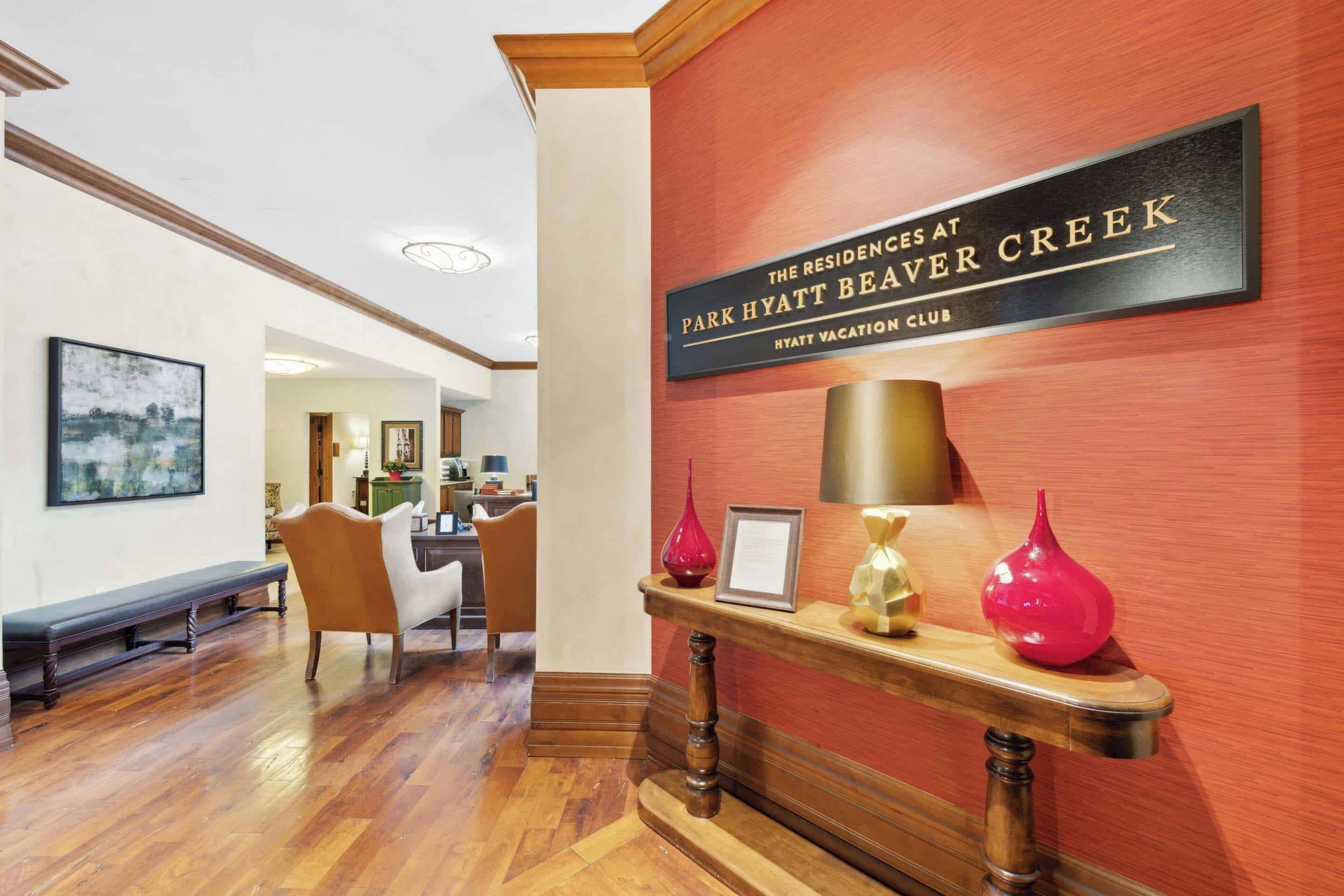 A hotel lobby with a wooden bench, a reception desk, and a sign indicating it's the residences at Park Hyatt Beaver Creek.