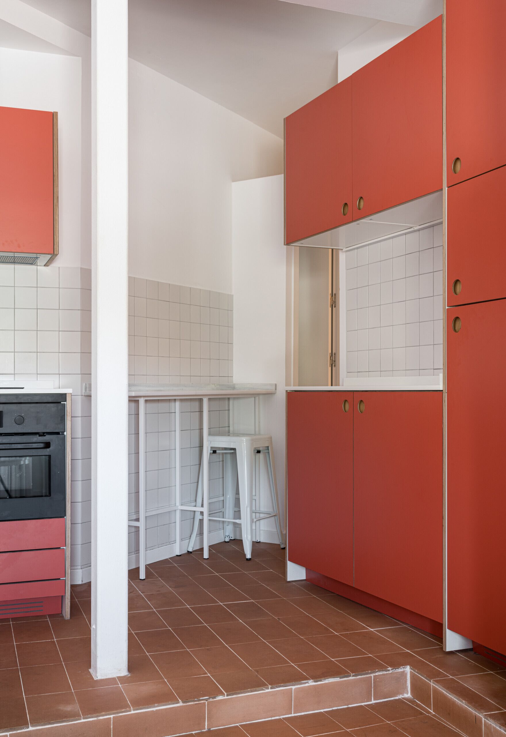 Una cocina con armarios blancos, un refrigerador rojo y un salpicadero de azulejos.
