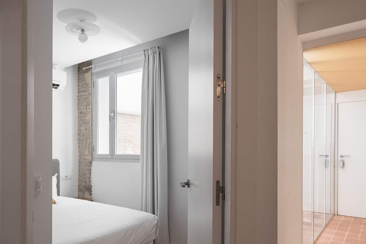 Ein Schlafzimmer mit Bett, Fenster und einer Tür, die auf einen Balkon führt.