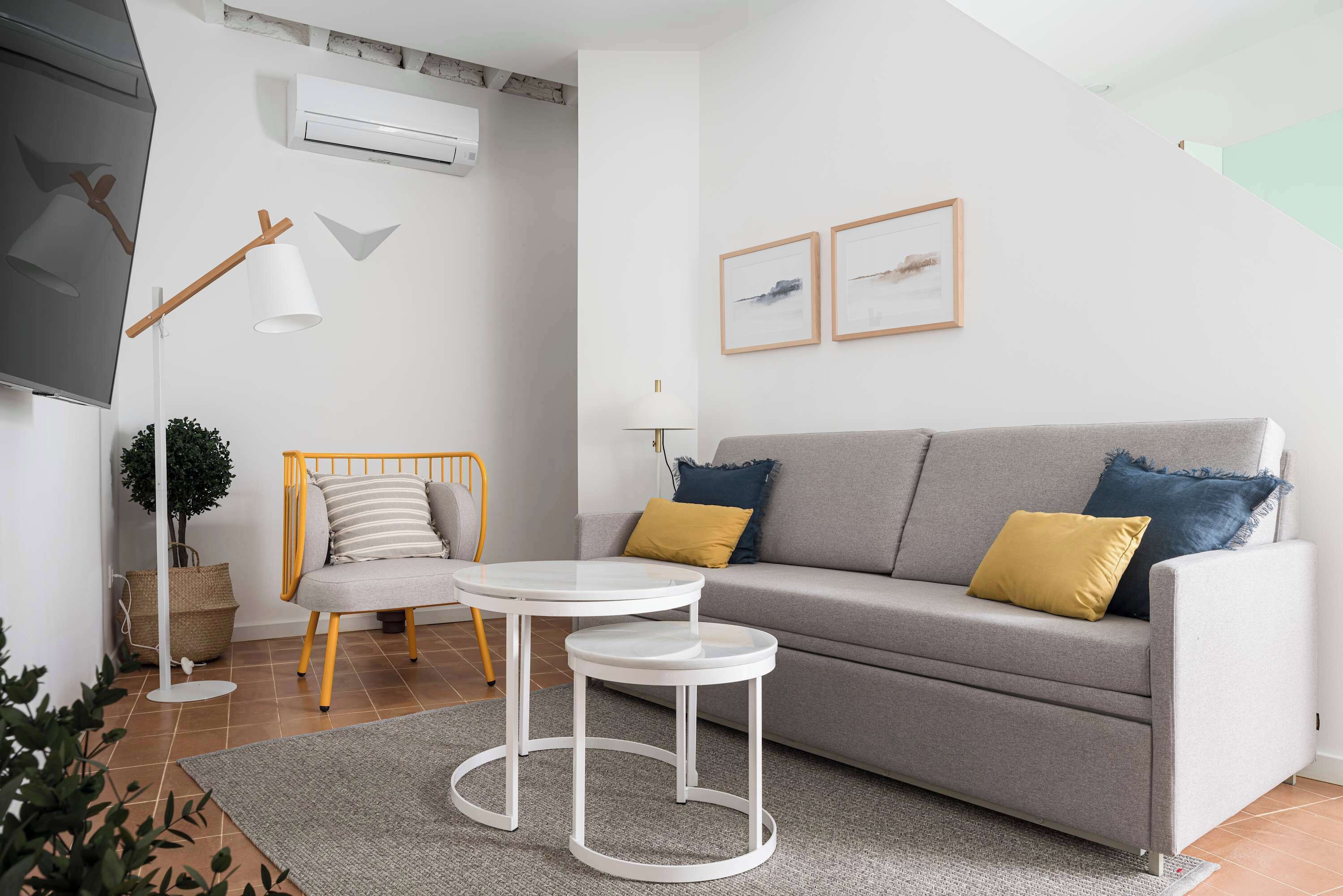 Un salon moderne avec un canapé gris, deux tables d’appoint, une lampe sur pied et un climatiseur fixé au mur.