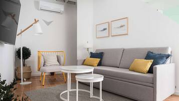 Un salon moderne avec un canapé gris, deux tables d’appoint, une lampe sur pied et un climatiseur fixé au mur.