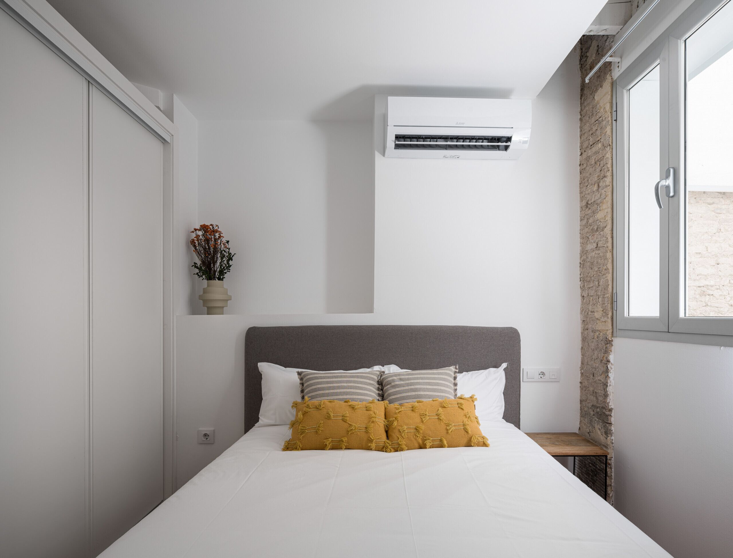 Una camera da letto con un letto, un condizionatore d'aria a muro, una piccola finestra e una pianta in vaso.