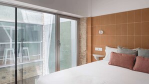 Ein Schlafzimmer mit einem großen Bett, einem Nachttisch, einer Wandleuchte und einer Glastür zum Außenbereich.