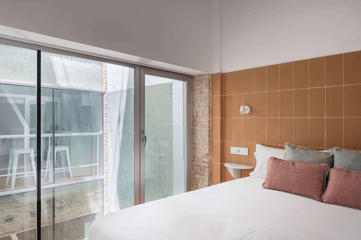 Ein Schlafzimmer mit einem großen Bett, einem Nachttisch, einer Wandleuchte und einer Glastür zum Außenbereich.
