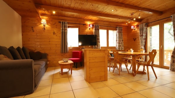Un interior de madera con un sofá, una silla roja, un televisor y una zona de comedor.