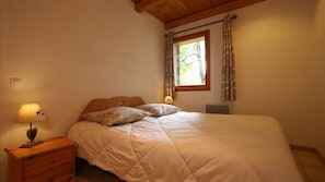 Un dormitorio con cama, mesita de noche con lámpara, ventana con cortinas y techo de madera.