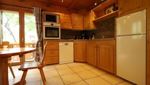 A wooden cabin kitchen with a dining table, chairs, a dishwasher, a refrigerator, and a microwave.