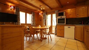 A wooden cabin interior with a dining table, chairs, a kitchen with a microwave and oven, and a dishwasher.