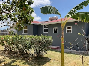 A two-story house with a red roof, a small front yard, and a visible solar panel on the roof. - Charming 2-bedroom house with WiFi, AC in delightful Christ Church (Christ Church)