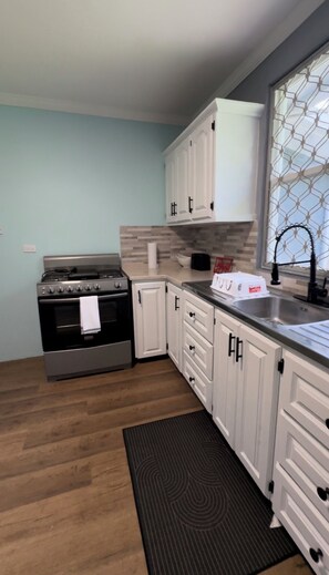 A kitchen with a stove, oven, white cabinets, and a window with a metal screen.