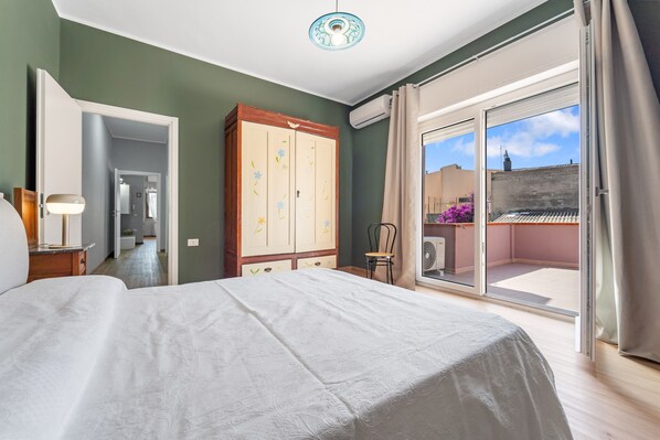 A bedroom with a bed, a wardrobe, a chair, and a balcony with a view.
