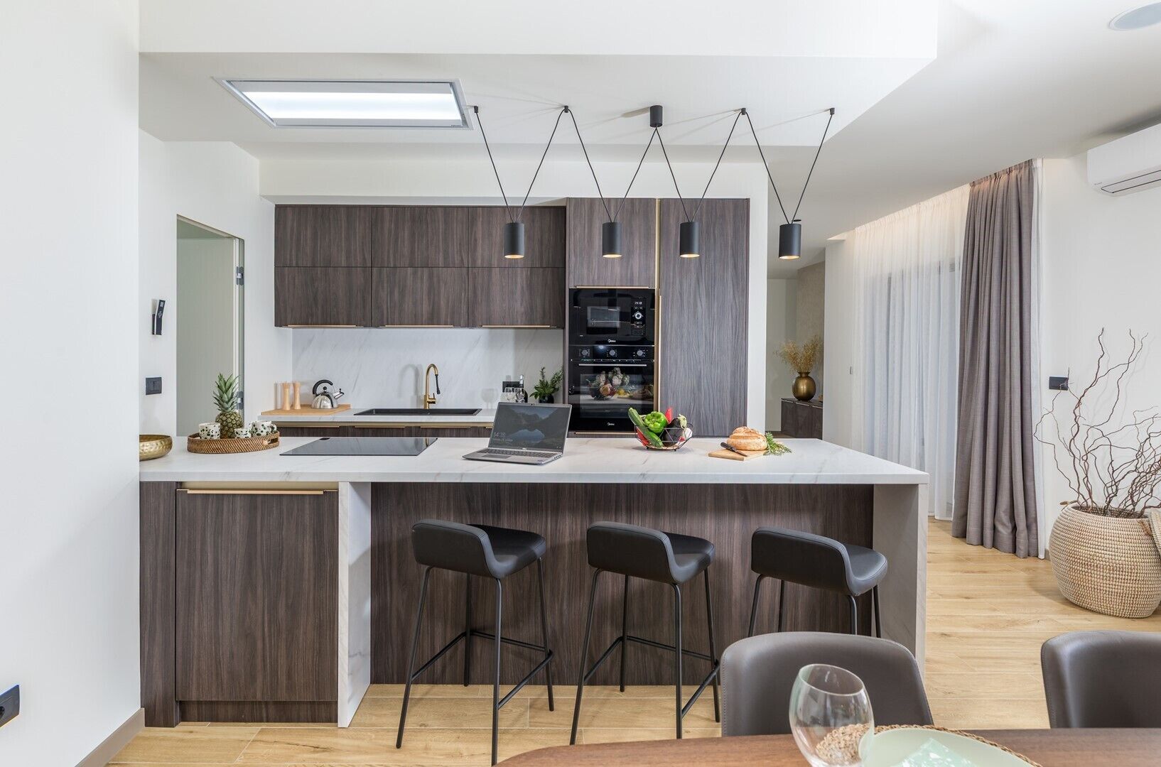 A modern kitchen with a central island, bar stools, a laptop, and a dining area with a table and chairs.