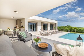 Un espace de vie extérieur moderne, doté d’une piscine, de chaises longues et d’un coin repas.