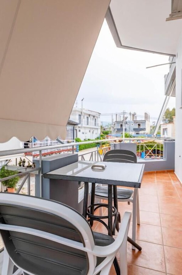 A balcony with a table and chairs, a view of buildings in the background, and a tiled floor.