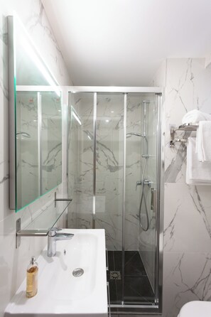 Une salle de bain moderne avec une douche en verre, un lavabo blanc et un mur recouvert de carreaux de marbre.